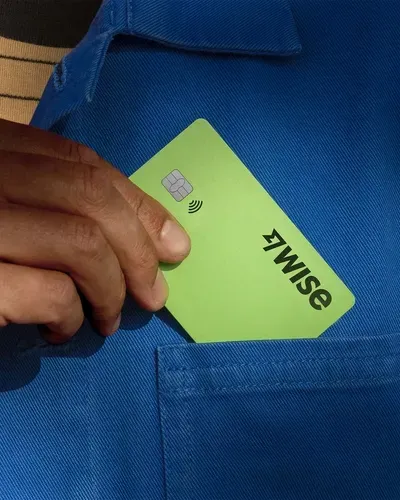 A hand slipping a green Wise debit card into a shirt pocket
