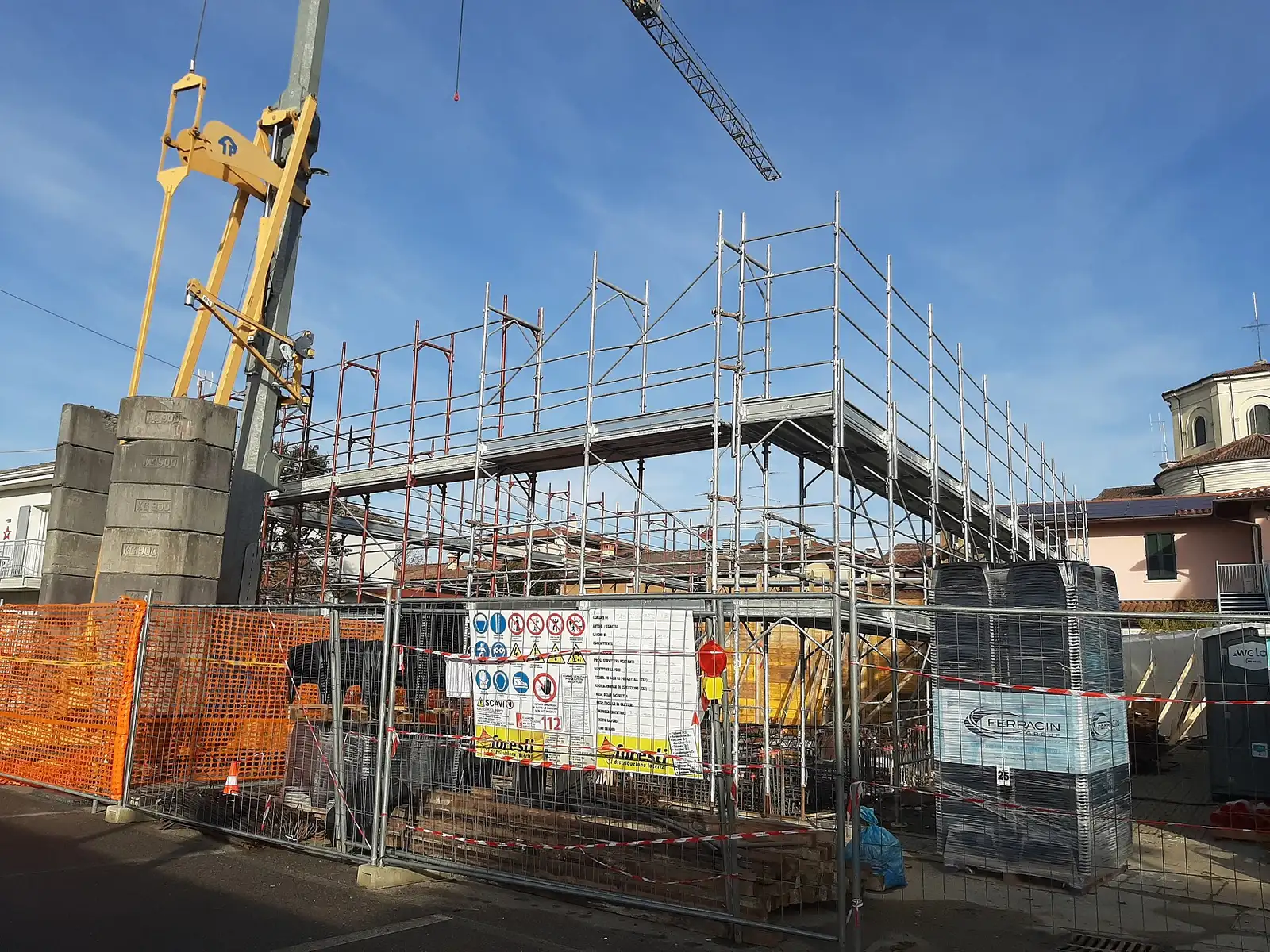 A building site in Castegnato, Italy, with scaffolding, a tower crane and the site notice board on the fence