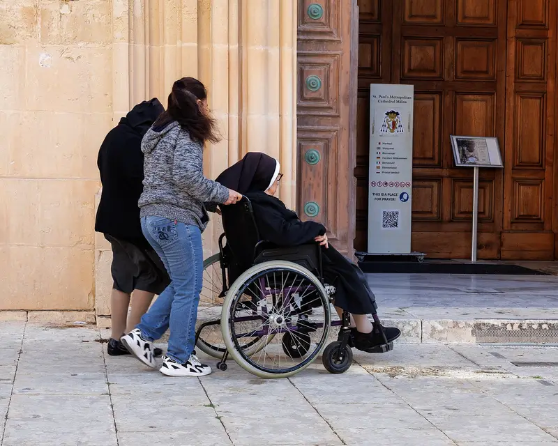 A carer, seen from behind, pushing an elderly woman in a wheelchair