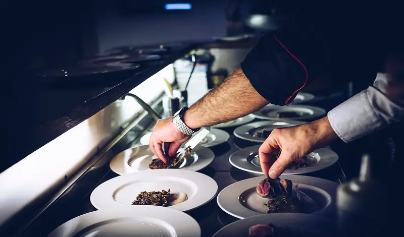 A chef's hands plating dishes in a restaurant kitchen in Italy