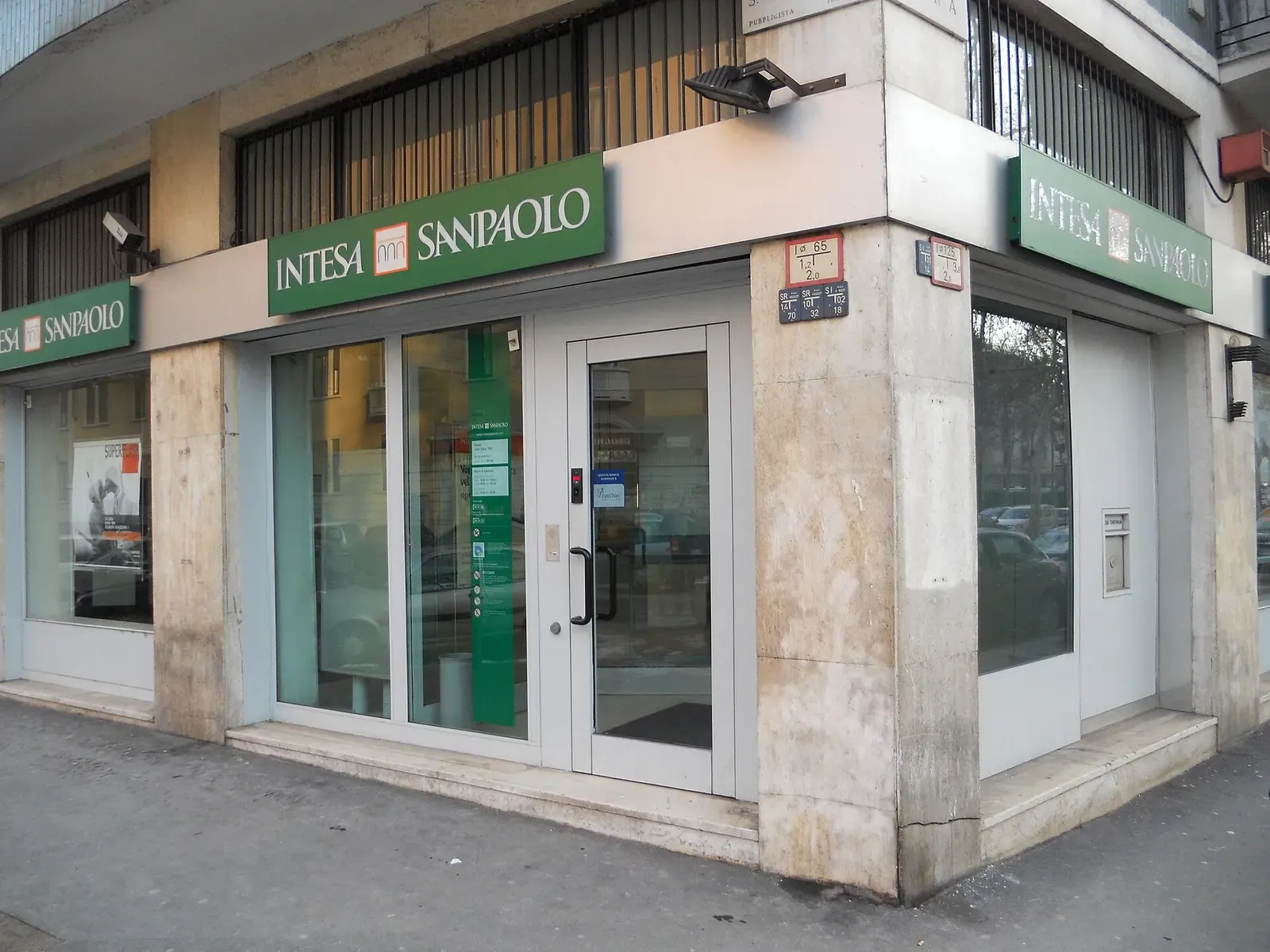 Corner entrance of an Intesa Sanpaolo branch in Italy, with green signs above glass doors