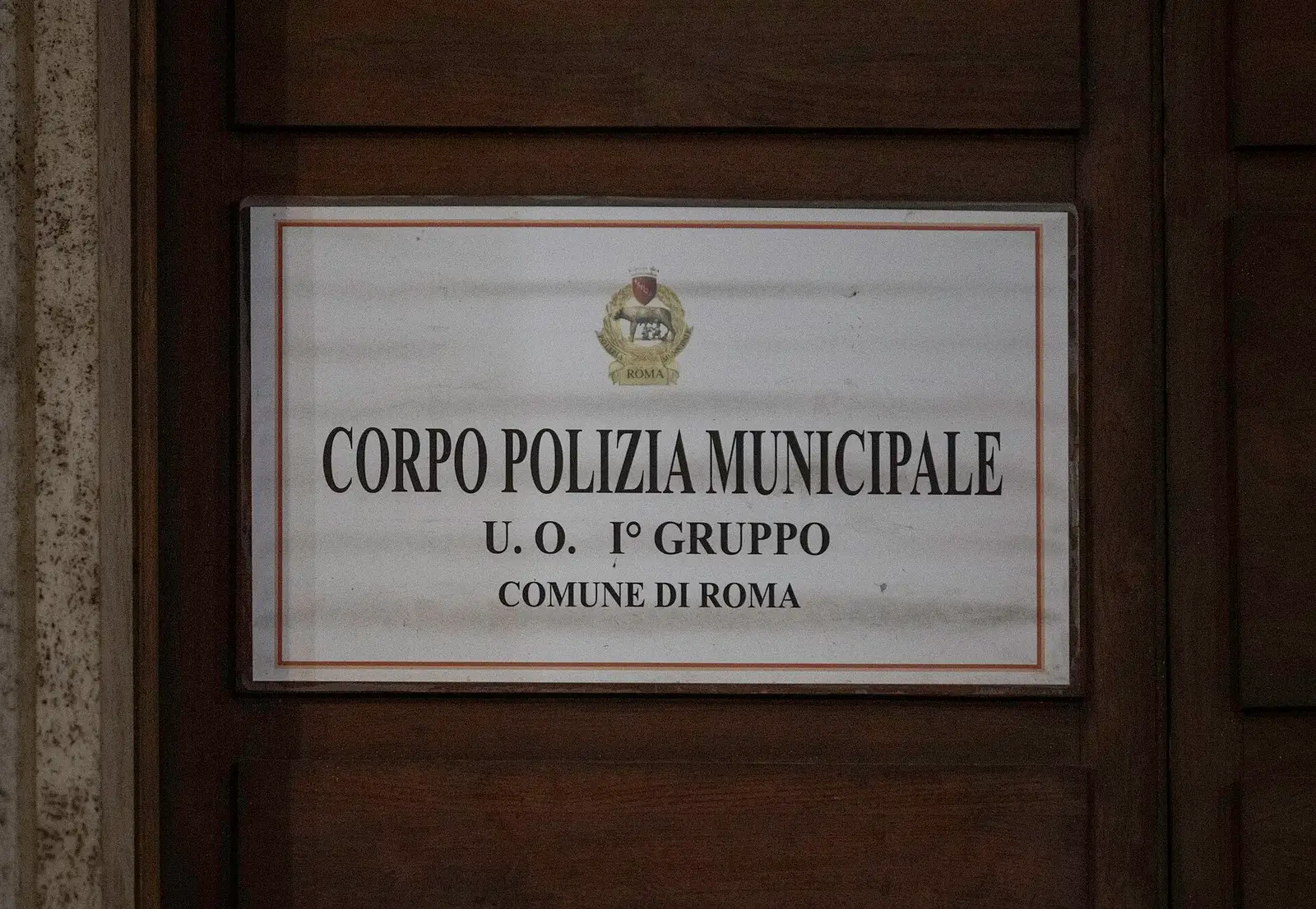 A white plaque on a wooden door reading Corpo Polizia Municipale, U.O. I Gruppo, Comune di Roma