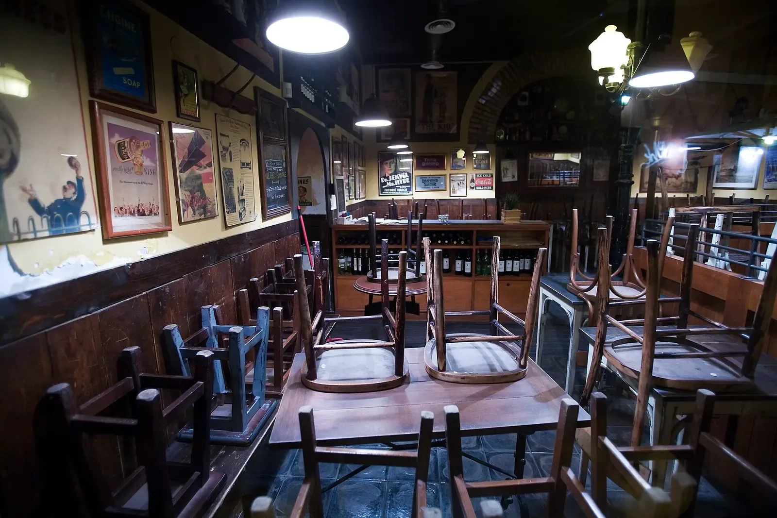 Inside an empty restaurant in Trastevere, Rome, with chairs stacked on wooden tables and old posters on the walls