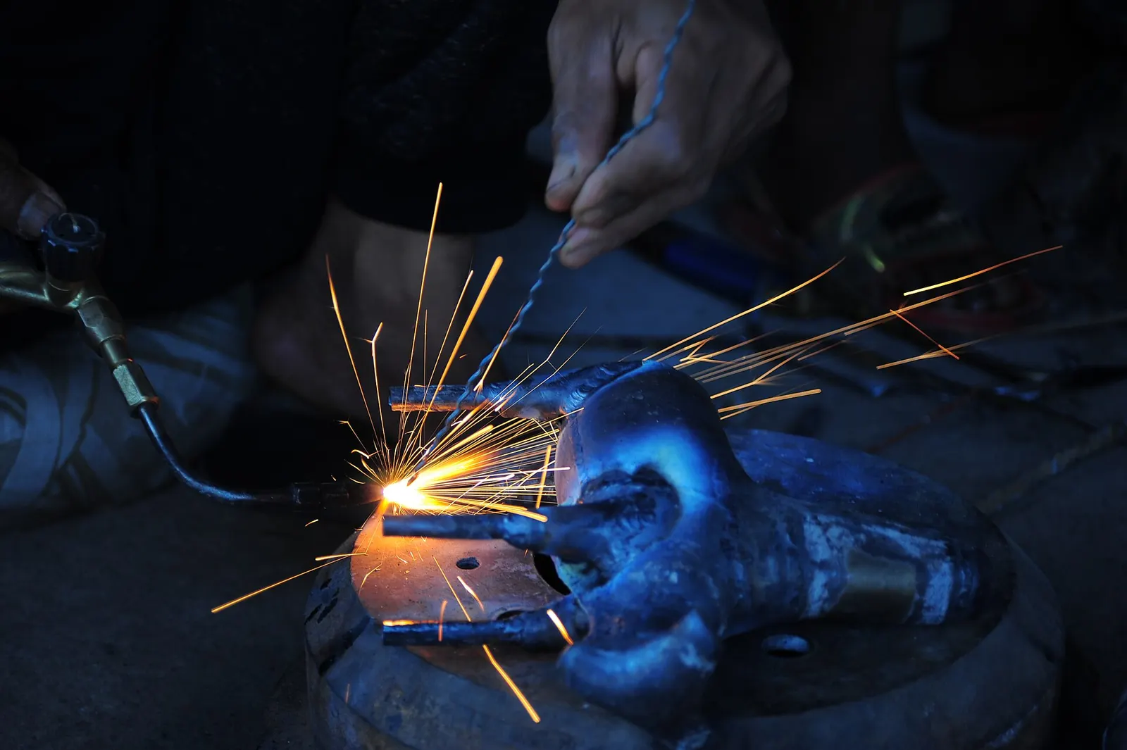 Close-up of hands gas-welding a metal part, with sparks flying